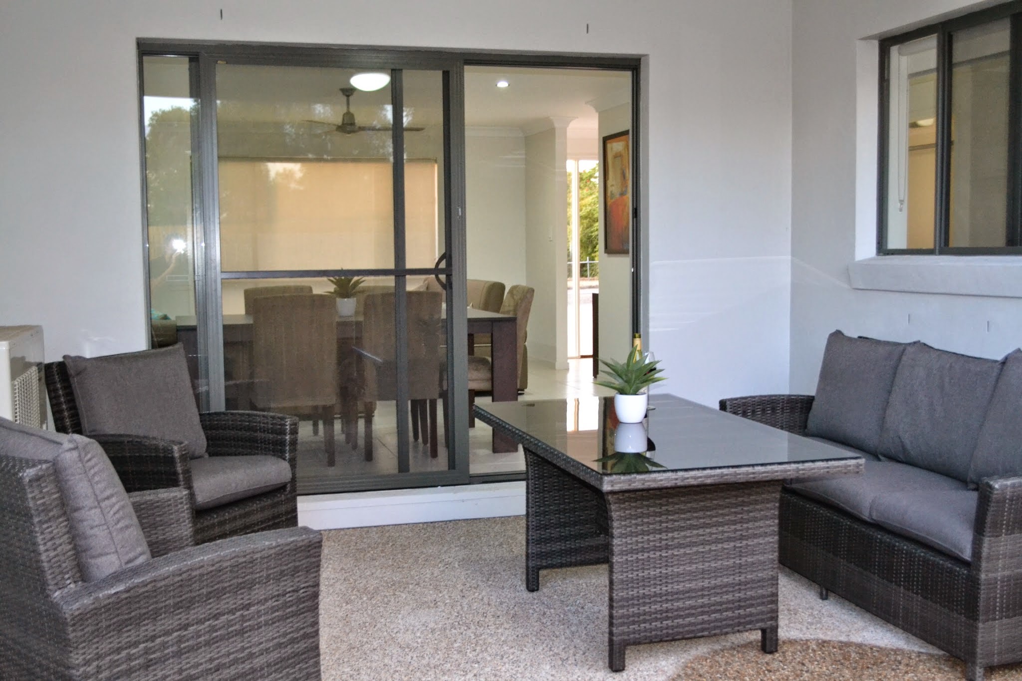 Covered terrace with a grey wicker outdoor lounge and dining table